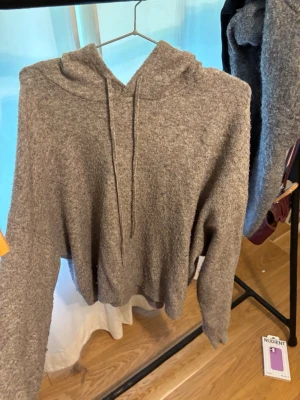 Mjuk gråmelerad hoodie med huva - En supermjuk och mysig gråmelerad hoodie med huva och dragsko. Tillverkad i ett fluffigt material som känns skönt mot huden. Perfekt för chill dagar eller när du vill ha något bekvämt och stilrent. Långärmad och avslappnad passform.