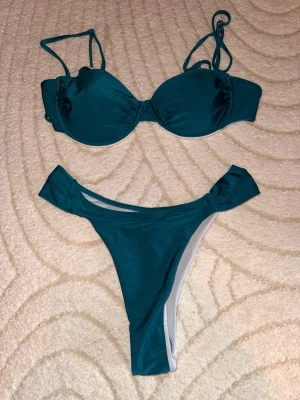 Mörkgrön bikini med bygel och band - Snygg mörkgrön bikini med vadderad bygel-bh och smala axelband. Bikinitrosan har hög skärning och breda sidor. Materialet är mjukt och stretchigt, perfekt för strandhäng eller poolen.Helt oanvända