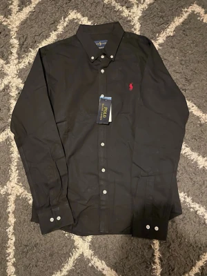 Svart skjorta från Polo Ralph Lauren - Klassisk svart skjorta från Polo Ralph Lauren. Helt ny och pris kan dikteras. TAR GÄRNA EMOT PRISFÖRSLAG.