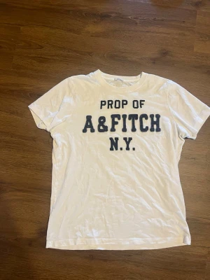 Vit Abercrombie Fitch tshirt - Säljer denna snygga tshirt då den har blivit för liten för mig! Tröjan har riktigt schysst passform skulle säga att den passar runt S/M och har inga defekter