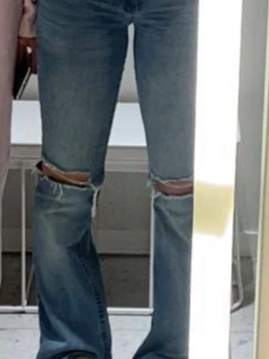 Blå bootcut jeans med slitningar - Säljer ett par ljusblå bootcut jeans med slitna hål vid knäna och broderade detaljer på bakfickorna. Jeansen har hög midja och är tillverkade i denim med lätt stretch. Perfekta för en avslappnad och trendig look.
