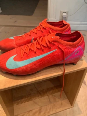 Röda Nike fotbollsskor med turkos swoosh - Säljer ett par grymma röda Nike fotbollsskor med turkos Nike logga på sidorna. Skorna har snörning, låg profil och är tillverkade i ett lätt syntetmaterial som ger bra bollkontroll. Perfekta för dig som vill sticka ut på planen! De funkar perfekt, har inga defekter eller nåt sånt, ser bara lite smutsiga ut ifrån planen. Använda ganska fåtal gånger. Säljer pga att jag ej spelar längre.                                            Pris ej helt fast.