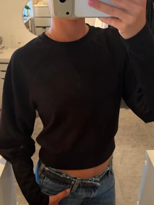 Svart sweatshirt - En enkel och stilren svart croppad sweatshirt med rund halsringning och långa ärmar. Lite tajtare runt magen om pösigare uppåt. Armarna är smalare nertill och även där puffigare uppåt. 