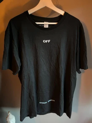 Svart Off-White t-shirt med tryck - Säljer en svart t-shirt från Off-White med vit text 'OFF' framtill och stort grafiskt tryck i blått och vitt på ryggen. T-shirten har rund hals och korta ärmar. Materialet är mjuk bomull och passformen är normal.