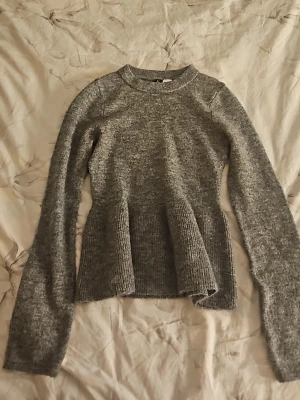 Grå stickad peplumtröja från H&M - Säljer en grå stickad tröja från H&M Divided med peplumdetalj nedtill. Tröjan har rund halsringning, långa ärmar och är gjord i mjukt, melerat material. Perfekt för dig som gillar en enkel men ändå trendig look.