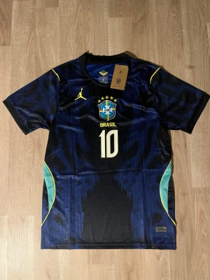 Brasilien Neymar Jr matchtröja #10 - Snygg svart och blå Brasilien matchtröja med Neymar Jr och nummer 10 på ryggen. Tröjan har gula detaljer, klubbmärke på bröstet samt gröna inslag på sidorna. Perfekt för dig som älskar fotboll och vill sticka ut på planen. HELT NY!