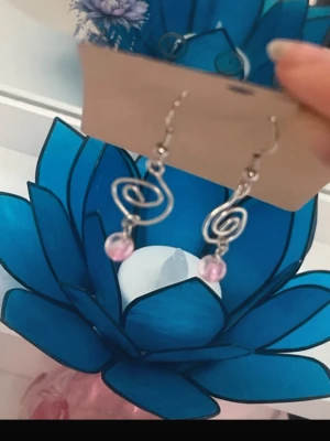 Handgjorda Silvriga örhängen med rosa pärlor - Handgjorda Örhängen i silver och rosa Handgjorda Örhängen i rostfritt stål Handgjorda örhängen i silverfärgad metall med spiralformad design och små rosa pärlor som hänger längst ner. 
