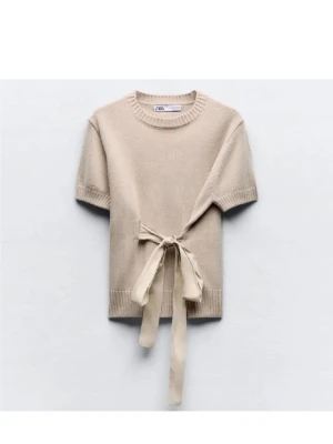 Beige stickad topp med knytband - Trendig beige stickad topp från Zara med korta ärmar och rund halsringning. Toppen har ett snyggt knytband i midjan som ger en cool detalj. Perfekt att styla med jeans eller kjol för en avslappnad look.