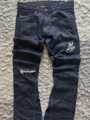 Bootcut jeans Remade - Crocker Bootcut Jeans – Handgjord Design – Väldigt bra skick  Riktigt snygga originaljeans från Crocker som jag själv gjort om till bootcut. Har lagt till egna slitningar, små unika detaljer samt designat om bakfickorna för ett mer exklusivt och personligt uttryck. Ett par jeans som verkligen sticker ut och är helt unika.  Storleken är 33/32, men jag rekommenderar att du utgår från måtten nedan för bästa passform.  📏 Mått: • Midja: 43 cm • Längd: 104 cm • Benöppning: 25 cm 