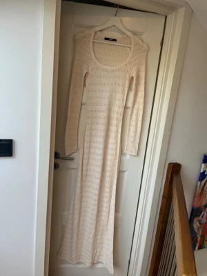Lång virkad klänning från Bik Bok - Lång, stickad strand klänning i bomull från Bik Bok i en ljus beige färg. Klänningen har lång ärm, rund ringning och ett genomgående hålmönster. 