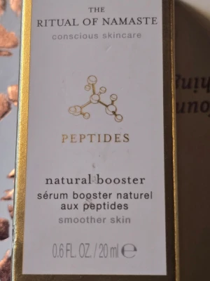 Rituals Peptides Natural Booster 20ml - Peptidserum från Rituals i serien The Ritual of Namaste. Kommer i en frostad glasflaska med pipett och guldfärgat lock. Innehåller 20 ml och är framtagen för att ge slätare hud. Förpackningen har eleganta guld- och vita detaljer. Pris i butik 269 kr