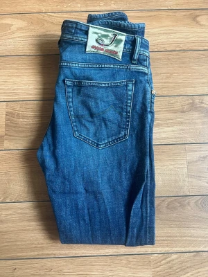 Mörkblå jeans från Jacob Cohen - Snygga mörkblå jeans från Jacob Cohen med klassisk femficksdesign och raka ben. Jeansen har en patch med logga bak på linningen och subtila slitningar framtill. Tillverkade i mjuk denim med snygg tvätt och detaljerade sömmar.