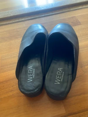 Svarta skinn-tofflor från Wera 37 - Stilrena svarta tofflor från Wera Stockholm i mjukt skinn. Klassisk slip-in modell med rundad tå och låg sula. Perfekta för en chill och avslappnad look hemma eller på språng. Snygg minimalistisk design som passar till det mesta. I skinn st 37. 