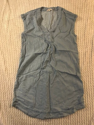 Ljusblå ärmlös topp med v-ringning - Snygg ljusblå ärmlös topp i mjukt bomullstyg med v-ringad hals och avslappnad passform. Perfekt till jeans eller shorts för en chill look. Enkel design utan mönster eller detaljer.