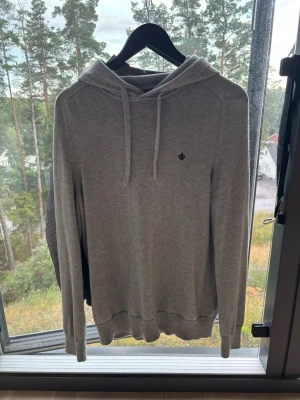 Grå hoodie från Morris Stockholm - Säljer en stilren grå hoodie från Morris Stockholm i storlek S. Hoodien har dragsko i huvan, ribbade muddar och en liten broderad logga på bröstet. Perfekt för dig som gillar en clean och enkel look.