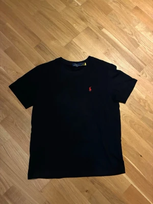 Polo Ralph Lauren t-shirt  - Klassisk svart t-shirt från Polo Ralph Lauren med röd broderad logga på bröstet. T-shirten har rund halsringning och korta ärmar. Tillverkad i mjuk bomull för en bekväm känsla och passar perfekt till alla tillfällen.