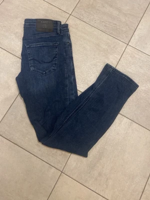 Mörkblå Slim Glenn jeans - Säljer ett par mörkblå Slim Glenn jeans med klassisk femficksdesign och slim passform. Jeansen har en snygg tvätt och är perfekta för dig som gillar en smalare siluett. 
