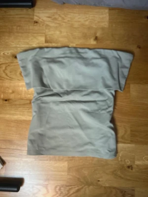 Beige axelbandslös tubtopp Forever 21 - Säljer en beige axelbandslös tubtopp från Forever 21. Toppen har en enkel och clean design, perfekt att styla med olika outfits. Materialet känns mjukt och stretchigt, vilket gör den bekväm att bära. Passar dig som gillar minimalistiska plagg.
