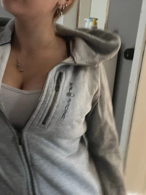 Ljusgrå hoodie från Sail Racing - Ljusgrå hoodie från Sail Racing med dragkedja framtill och en extra bröstficka med dragkedja. Broderad logga på bröstet och stor huva.  Obs: Kan bara skicka med Bring eller Postnord! Pris kan diskuteras!