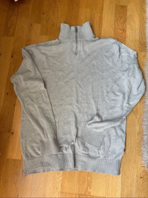 Jack & Jones Quarter Zip – Grå (StrL M) - Säljer en ljusgrå tröja från Jack & Jones med quarter zip och hög krage. Tröjan har långa ärmar, ribbade muddar och nederkant. Perfekt för lager på lager och enkel att matcha med olika outfits.