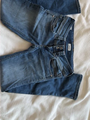 Blå jeans från Pepe Jeans Power Flex - Säljer ett par blå jeans från Pepe Jeans Power Flex med två knappar i midjan och klassisk femficksdesign. Jeansen har en lätt tvättad look och smal passform. Perfekta för dig som gillar stretchigt material och snygg vardagsstil.