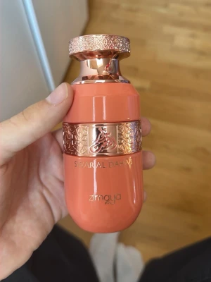 Swarial Dahab parfym från Zimaya - Säljer en Swarial Dahab parfym från Zimaya. Flaskan är korallfärgad med detaljer i roséguld och har ett elegant mönster runt mitten. Snygg och unik design som sticker ut i parfymhyllan.