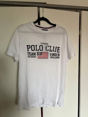 Vit t-shirt från Vinson Polo Club - Vit t-shirt från Vinson Polo Club med tryck framtill i svart och amerikansk flagga. Ny med lappen kvar!