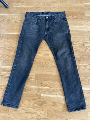 Svarta slim fit jeans med slitningar - Snygga svarta slim fit jeans med diskreta slitningar och klassisk femficksdesign. Jeansen har vita kontrastsömmar och en liten logodetalj på fickan. Passar perfekt till en avslappnad streetwear-look och är tillverkade i mjuk denim.