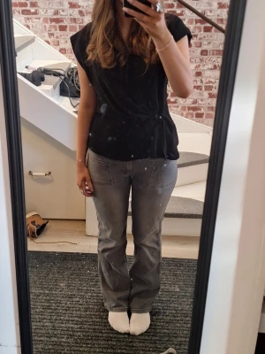 Svart omlottopp med v-ringning - Snygg svart omlottopp med v-ringning och korta ärmar. Toppen har en lätt draperad effekt vid midjan och en enkel, stilren look. Perfekt att matcha med jeans eller kjol för en trendig outfit.