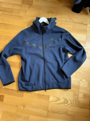 Mörkblå Tracksuit från Nike - Säljer ett Nike Tech Fleece-set i marinblått. Inkluderar hoodie med dragkedja och matchande byxor. I fint skick och fungerar perfekt till både vardag och träning.