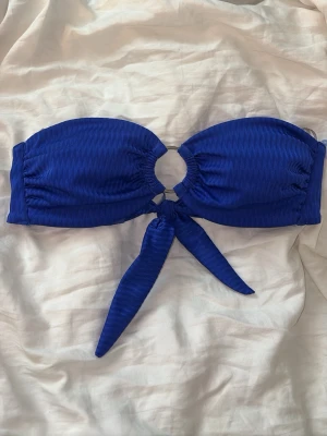 Blå bandeau bikiniöverdel med knyt - Snygg bandeau bikiniöverdel i starkt blå färg med subtila ränder. Toppen har en ringdetalj framtill och knytband vid ryggen💙