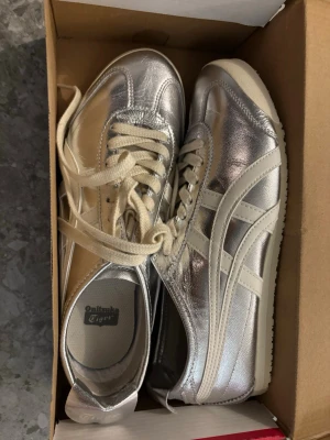Silvriga Onitsuka Tiger sneakers - Säljer ett par riktigt snygga Onitsuka Tiger sneakers i metallic silver med vita detaljer och vita snören. I modellen Mexico 66. Helt oanvända, köpta i deras butik i Japan. 