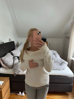 Vit off shoulder stickad tröja - Säljer en mjuk och fluffig vit stickad tröja med bred off shoulder-krage och långa ärmar. Tröjan har ribbstickade muddar vid ärmslut och nederkant, perfekt för en trendig och mysig look.