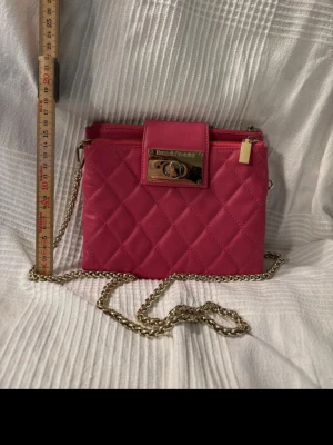 Rosa quiltad handväska i skinn Russell & Bromley (Made in Italy) - Snygg rosa quiltad handväska i skinn från Russell & Bromley (Made in Italy), med guldfärgad kedjerem och vridlås i metall. Väskan har ett elegant rutmönster och dragkedja upptill. Kedjan kan tas av och väskan användas som clutch. Guldskylten har någon repa men väskan har inga skav utan är i fint skick. Perfekt för dig som vill ha en färgklick till din outfit.