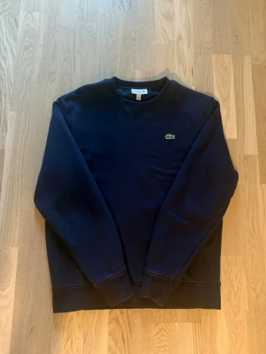 Mörkblå sweatshirt från Lacoste - Säljer en mörkblå tröja från Lacoste, den är i bra skick. Storlek L men skulle säga att den är lite mer åt M hållet. Hör av dig om du har några frågor eller funderingar 
