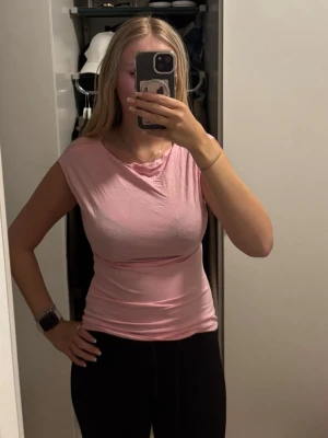 Ljusrosa ärmlös topp - Säljer en ljusrosa topp med tight passform och rund halsringning. Toppen är ärmlös och gjord i mjukt bomullsmaterial, perfekt för varma dagar eller som layering-piece. Enkel och stilren design som passar till det mesta.(den är inte strykt)