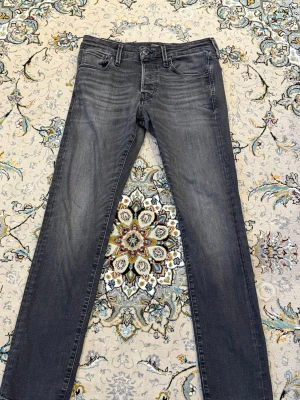 Mörkgrå slim fit jeans - Snygga mörkgrå slim fit jeans från Jack and Jones med klassisk femficksdesign, storlek 30/30. Jeansen har normal midja och raka ben, perfekta för en avslappnad men ändå stilren look. Tillverkade i stretchigt denimtyg för extra komfort.