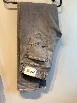 Replay grå slim fit jeans - Snygga grå jeans från Replay i slim fit-modell. Jeansen har klassisk femficksdesign, diskreta slitningar och tydliga sömmar på bakfickorna. Perfekta för dig som gillar en modern och stilren look.