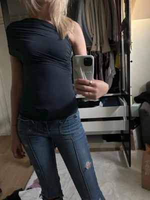 Mörkblå oneshoulder topp - Säljer en mörkblå oneshoulder topp med tight passform. Toppen har en asymmetrisk axel och är tillverkad i ett stretchigt material som sitter snyggt på kroppen. Perfekt för dig som vill ha en stilren och trendig look. Ej använd