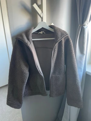 Brun teddyjacka med dragkedja - Mysig brun teddyjacka med dragkedja framtill och breda ärmar. Jackan har en avslappnad passform och är gjord i fluffigt teddy-material som håller dig varm. Perfekt för kyliga dagar och enkel att matcha med olika outfits.