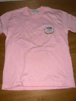 Rosa t-shirt från Casablanca - Säljer en rosa t-shirt från Casablanca med tryck fram och stort grafiskt tryck på ryggen. T-shirten har rund hals och korta ärmar. Materialet är mjuk bomull och passformen är normal. Perfekt för dig som gillar streetwear och snygga detaljer.