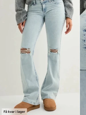 Ljusblå bootcut jeans med slitningar - Säljer ett par ljusblå bootcut jeans med slitna detaljer över knäna. Jeansen har låg midja och klassisk femficksdesign. Perfekta för dig som gillar en avslappnad och trendig stil. de står inte storlek men antingen s eller m