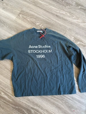 Svart långärmad topp Acne Studios - Cool svart långärmad topp från Acne Studios med tryck 'STOCKHOLM 1996' framtill. Klassisk rund halsringning och relaxed fit. Perfekt till jeans eller kjol för en avslappnad look.
