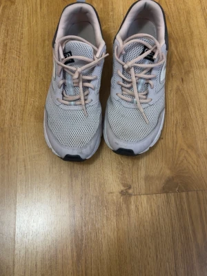 Ljusgrå mesh sneakers med svarta detaljer - Snygga sneakers i ljusgrå mesh med ljusrosa snören och vita samt svarta detaljer. Skorna har en sportig design med ventilerande ovandel och svart hälparti. Sulan är vit med svarta inslag undertill. Perfekta för en aktiv vardag.