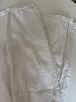 Vita linnebyxor med resårmidja - Säljer ett par luftiga vita linnebyxor med resår i midjan och raka ben. Perfekta för varma dagar och enkla att matcha med olika toppar. Materialet är linne vilket ger en skön och sval känsla.