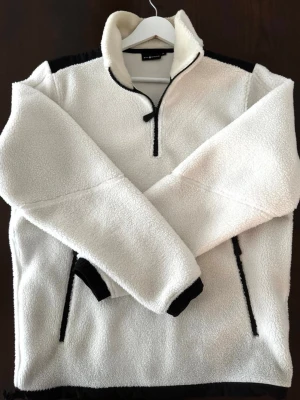 Vit fleece-tröja med dragkedja - Mysig vit fleece-tröja från Sail Racing i storlek M. Tröjan har halv dragkedja framtill, svarta detaljer vid dragkedja och axlar samt två fickor med dragkedja. Perfekt för kalla dagar och riktigt skön att ha på sig.