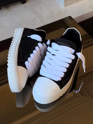 Svarta sneakers från Numeris - Säljer ett par svarta sneakers från Numeris med chunky vit sula och breda vita skosnören. Ovandelen är i svart tyg med vita kontrastsömmar och detaljer, samt en modell med vit-svart mönster. Klassisk låg modell med rund tå och kraftig yttersula.