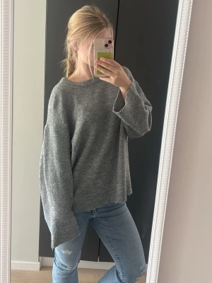 Oversized grå stickad tröja - Mysig oversized stickad tröja i grått med rund halsringning och långa, vida ärmar. 