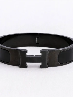Svart metallarmband med H-detalj - Snyggt svart armband i metall med en stor H-formad detalj framtill. Armbandet har en stilren och modern design med blanka svarta partier och mattsvart finish. Perfekt accessoar för dig som gillar minimalistisk och edgy stil.