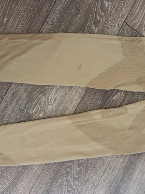 Beige leggings med mönster - Snygga beige leggings med diskreta geometriska mönster i olika nyanser av beige. De har en tight passform och är tillverkade i ett stretchigt material som sitter skönt på kroppen. Perfekta för en avslappnad och trendig look.